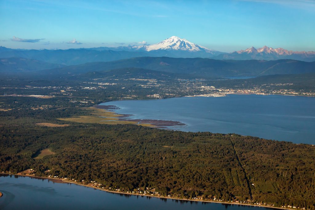 Aerial photo of Bellingham, showing the city and houses in the foreground, along with Puget Sound, and Mount Baker in the background.