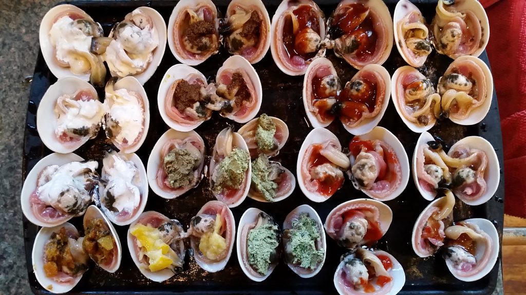 Close-up photo of a tray full of butter clams, garnished with various toppings, ready to be grilled.