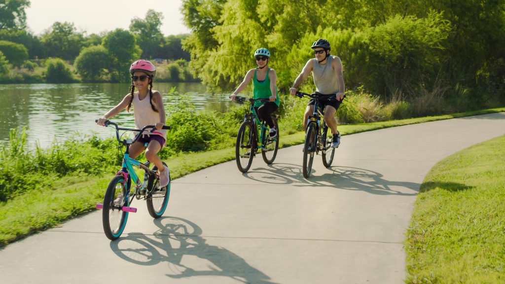 Photo of a family biking together along the path next to the Mission Reach section of the San Antonio River.