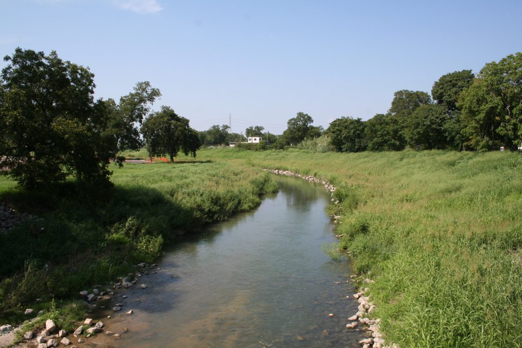 Photo of Mission Reach section of the San Antonio River before restoration, showing a low-flow river with very little tree cover on its banks. Photo credit: San Antonio River Authority.