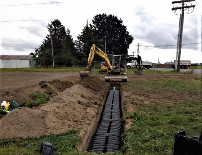 Photo of an excavator digging a new drain field for a residential septic system.