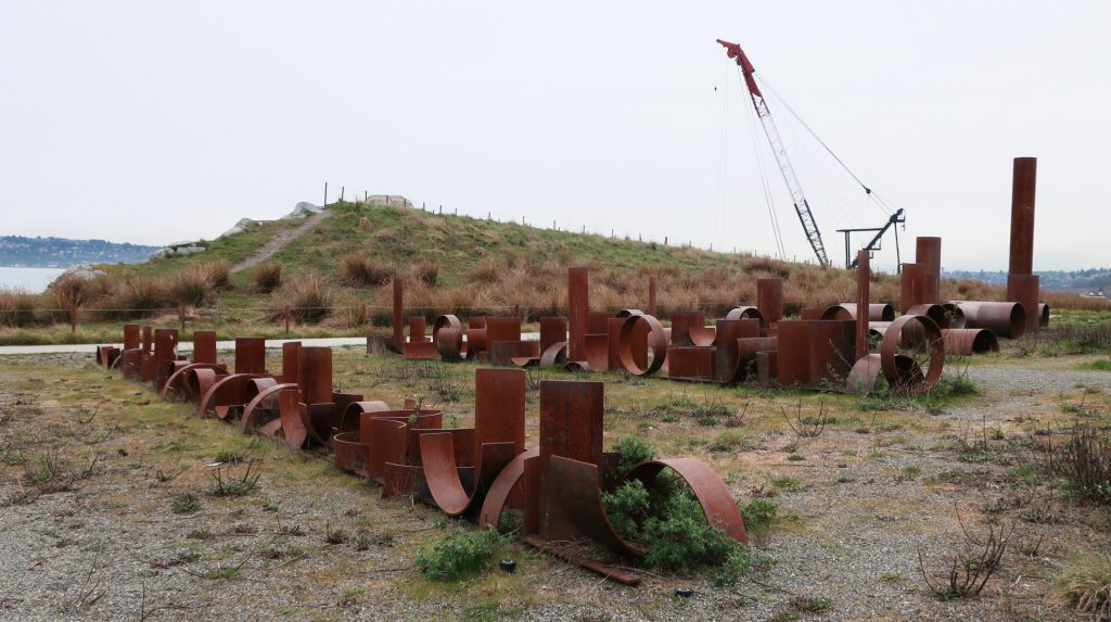 Photo showing the "Alluvion" artwork by Adam Kuby in Dune Peninsula Park. The artwork consists of a vertical steel pipe, meant to evoke the smelter smokestack, cut into smaller and smaller segments.