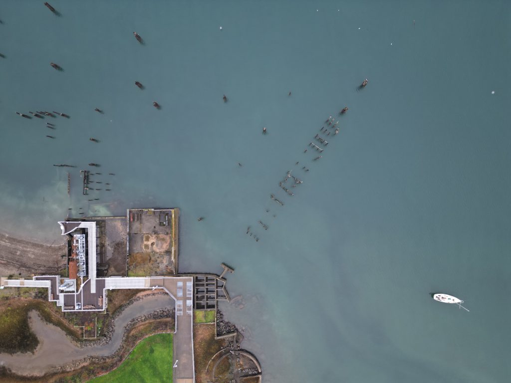 Aerial photo of the Dickman Mill site in Tacoma, WA. The photo shows the group of creosote-soaked pilings in the water near the site, and a boat floating in the water off to the righthand side of the photo.